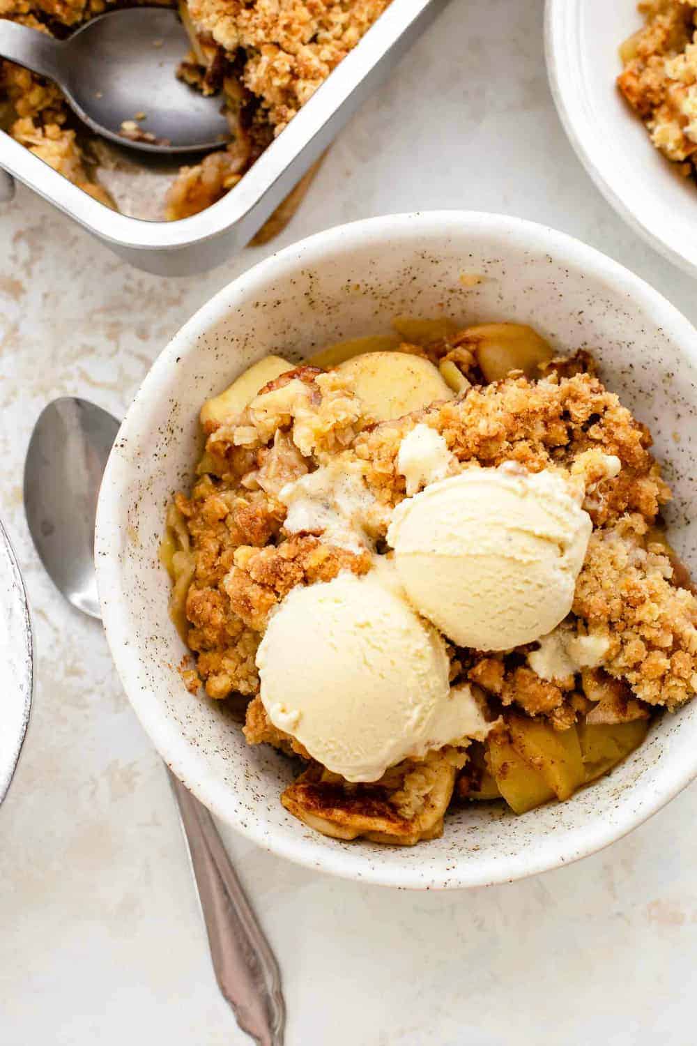 Spoon next to a small bowl of old fashioned apple crisp, topped with vanilla ice cream