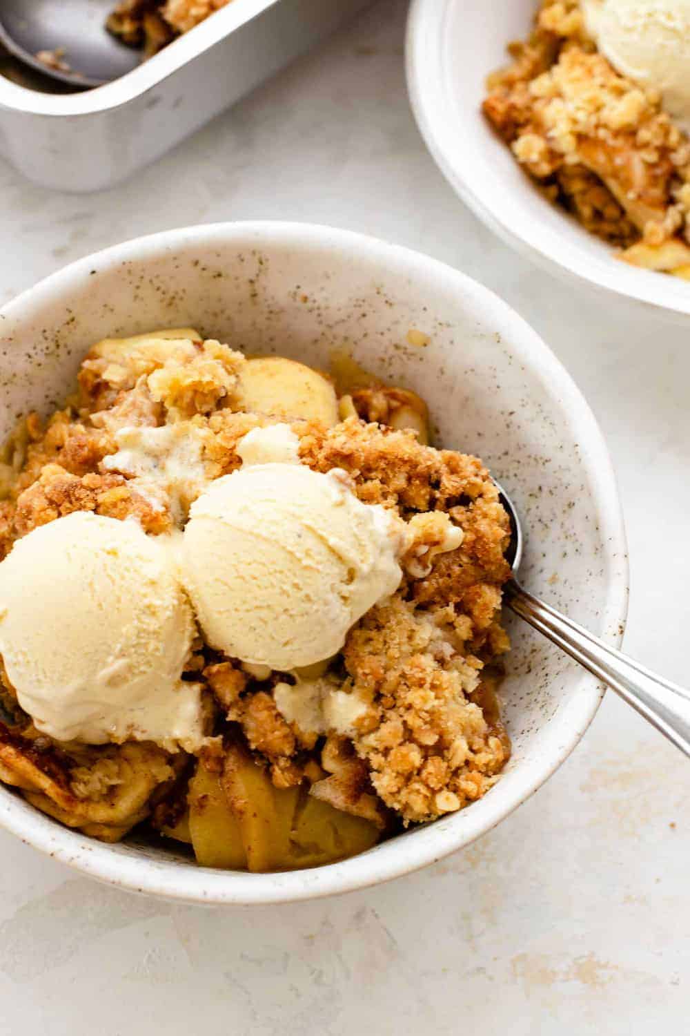 Old fashioned apple crisp in a small white bowl, topped with ice cream