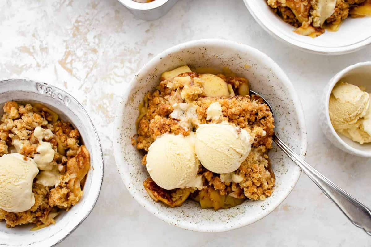 Small bowls of old fashioned apple crisp topped with scoops of vanilla ice cream