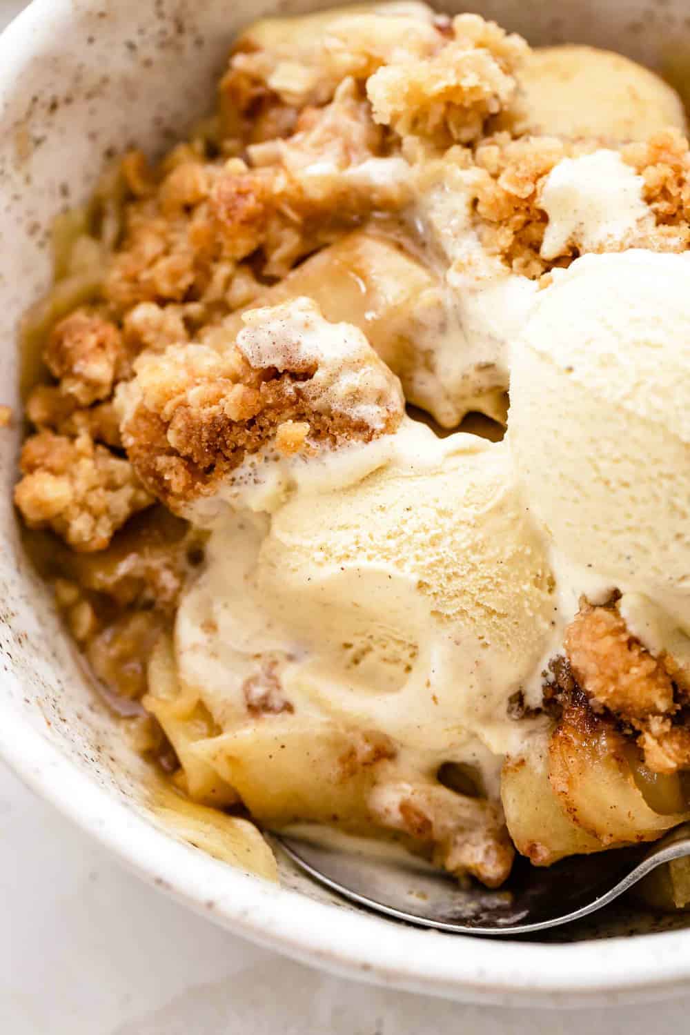 Close up of old fashioned apple crisp in a bowl, with vanilla ice cream on top