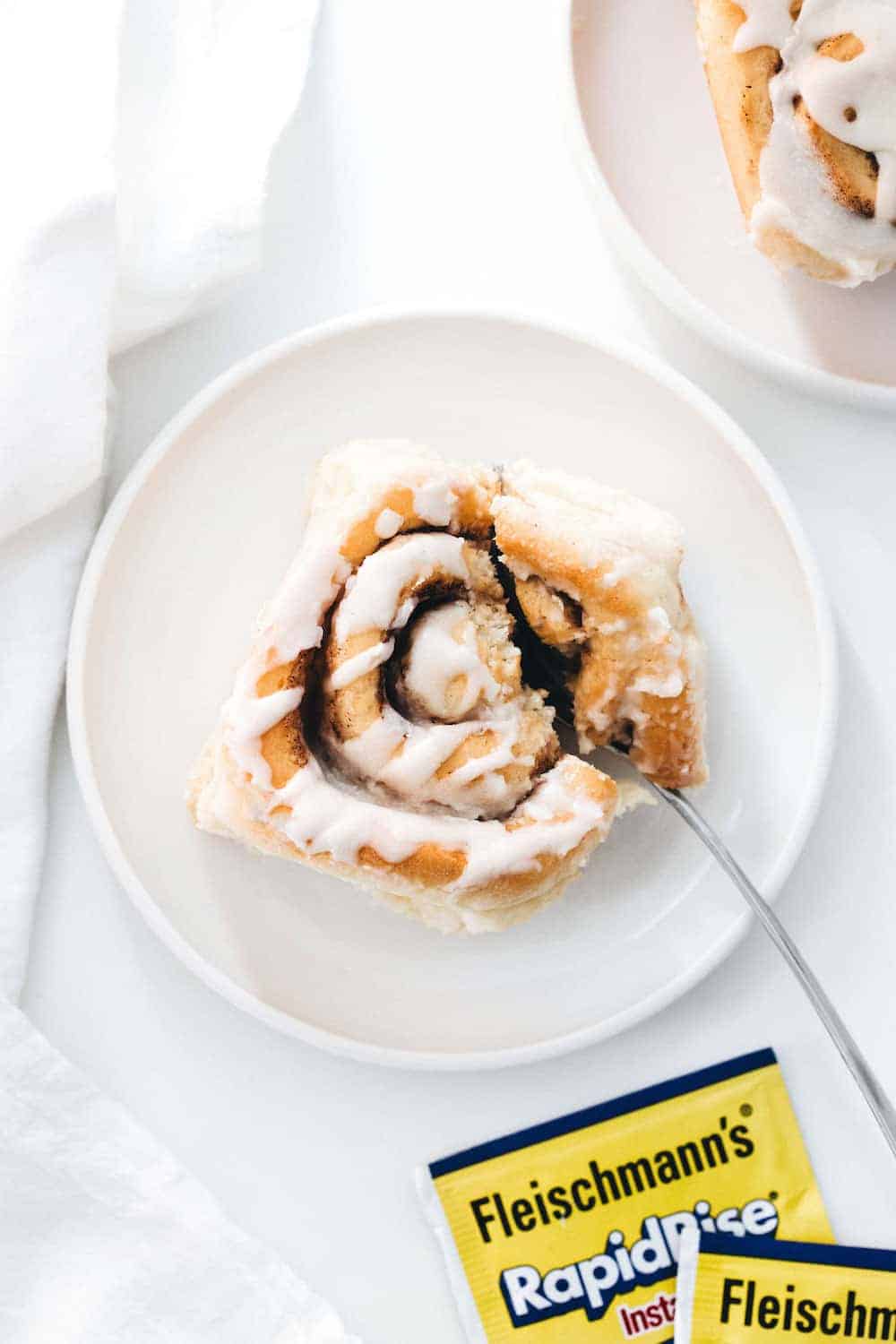 Maple Chai Cinnamon Roll on a white plate being cut with a fork