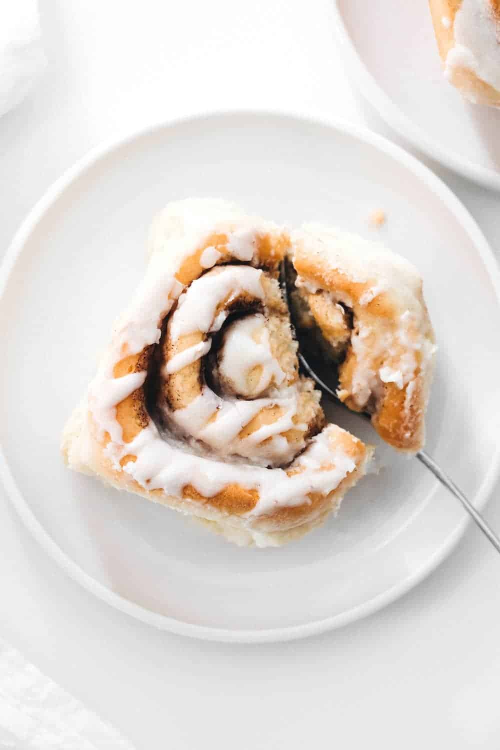 Chai cinnamon roll with maple frosting on a white plate with a fork