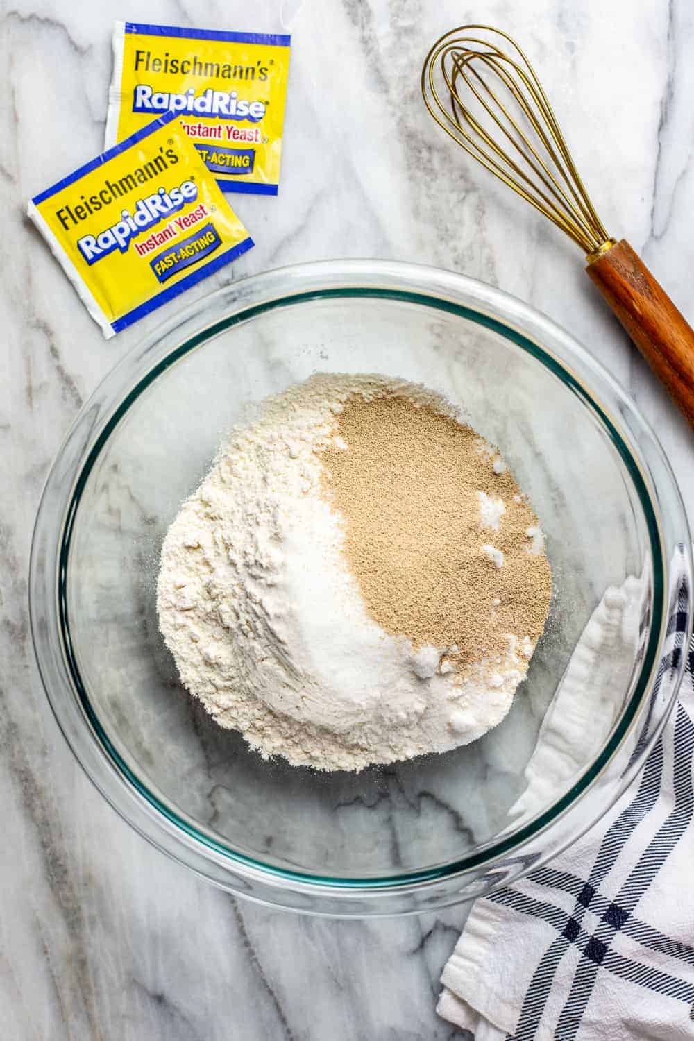 Dry ingredients for parker house roll dough in a glass mixing bowl on a marble surface