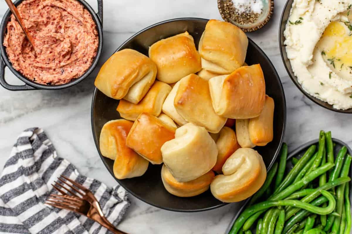 Bowl of parker house rolls next to a bowl of cranberry butter and other thanksgiving side dishes