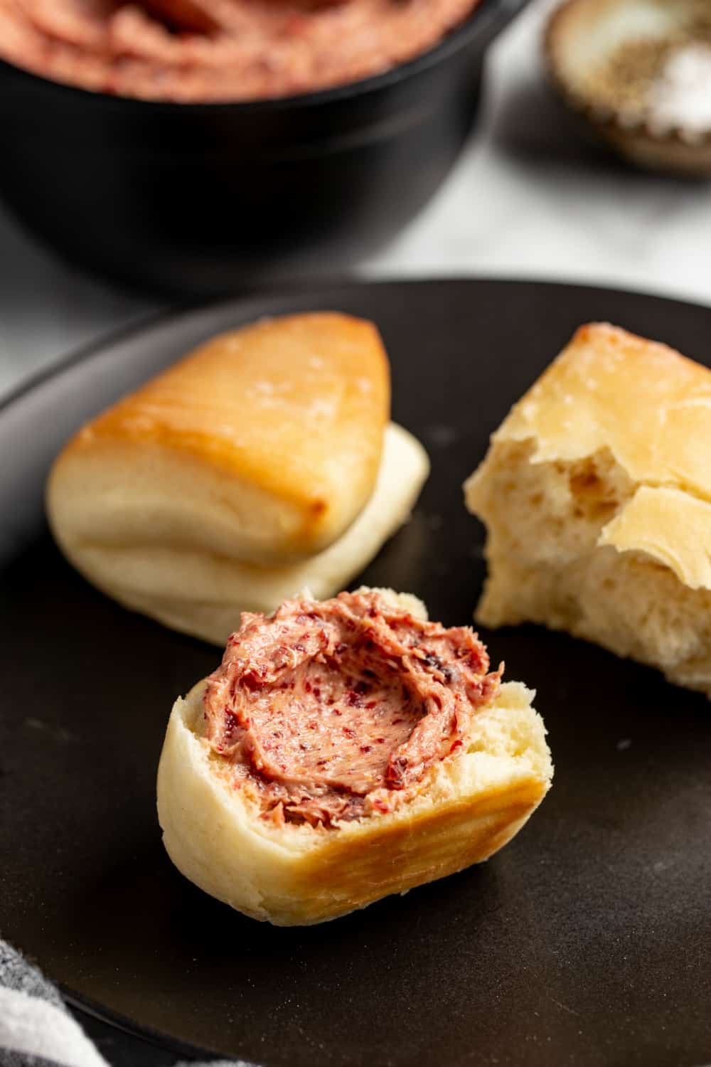 Parker house rolls on a plate, with one roll cut in half and spread with cranberry butter
