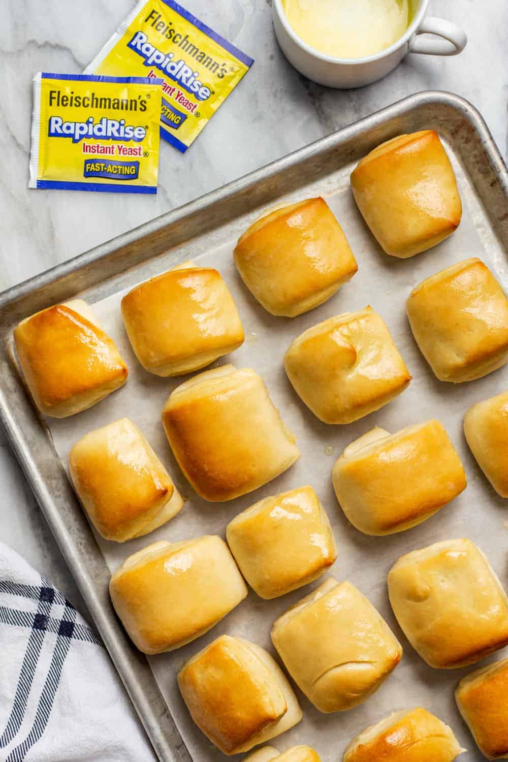 Baked parker house rolls on a baking sheet, freshly brushed with butter