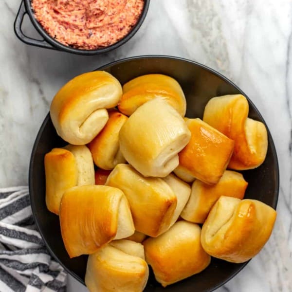 Parker house rolls in a bowl, next to a small bowl of cranberry butter