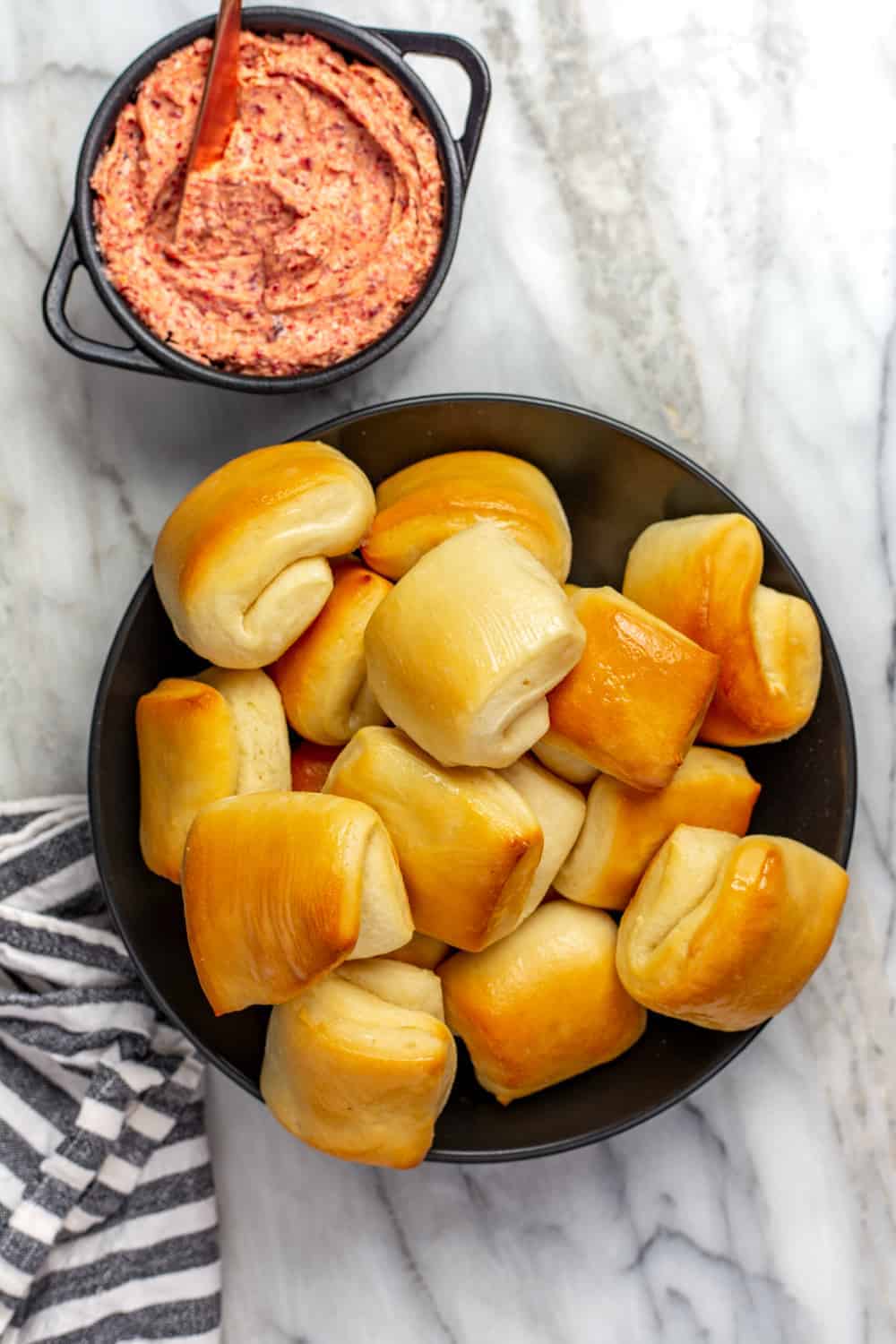 Parker house rolls in a bowl, next to a small bowl of cranberry butter