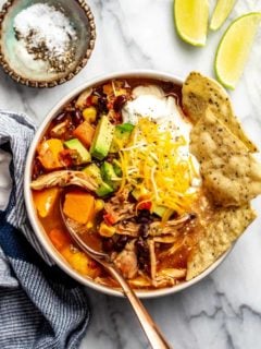Bowl of tortilla soup made with rotisserie chicken. Garnished with tortilla chips, cheese and sour cream