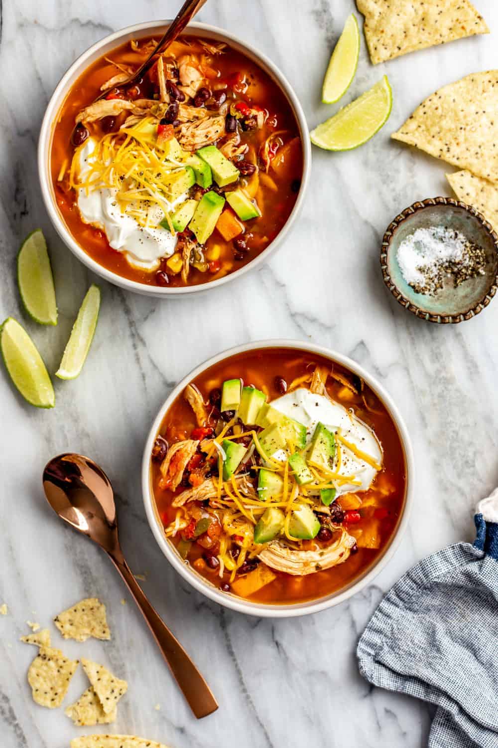 Two bowls of tortilla soup made with rotisserie chicken, garnished with tortilla chips, sour cream and served alongside lime wedges