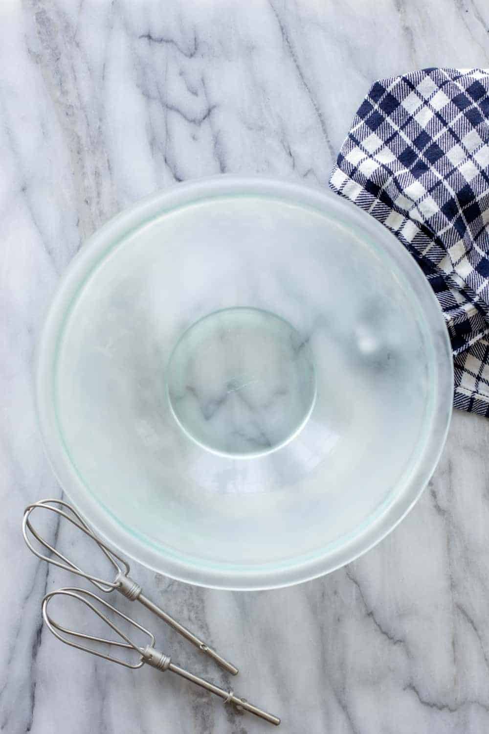 Cold glass mixing bowl and beaters on a marble counter