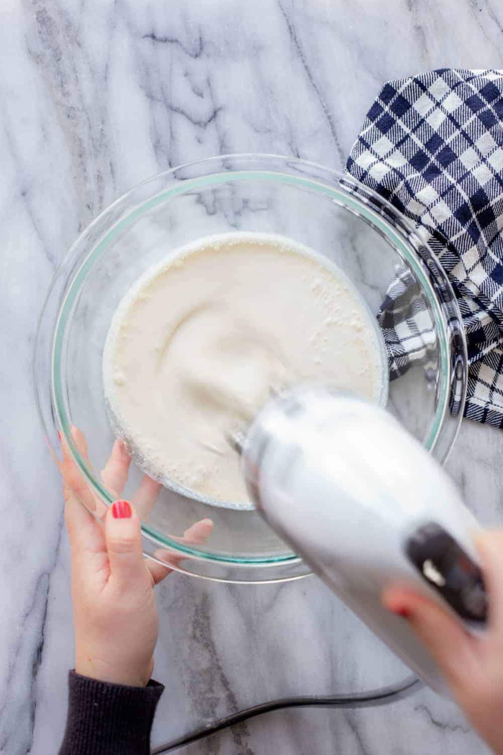 Hand mixer mixing a bowl of heavy cream to make whipped cream