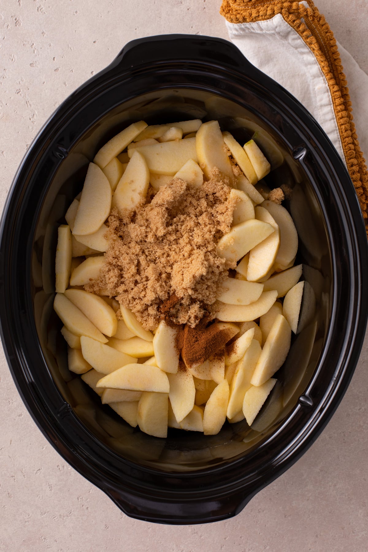 Sliced apples, brown sugar, and apple pie spice in the crock of a slow cooker.