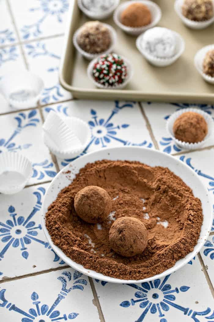 Two rum balls being rolled in cocoa powder