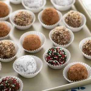 Rum balls with assorted toppings in paper liners, arranged on a sheet tray