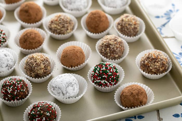 Rum balls with assorted toppings in paper liners, arranged on a sheet tray