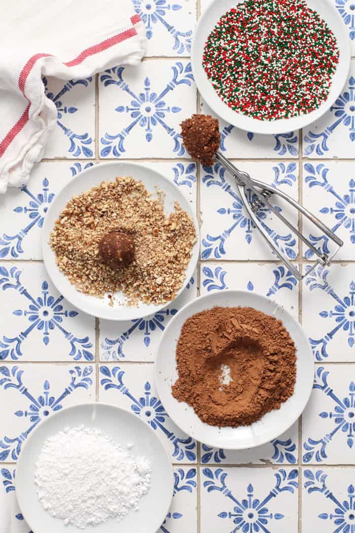 Rum balls being shaped with a cookie scoop and rolled in crushed pretzels and cocoa powder