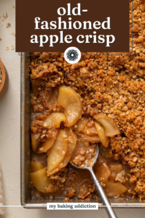Spoon in the corner of a pan of apple crisp, ready to scoop a portion out. Text overlay includes recipe name.