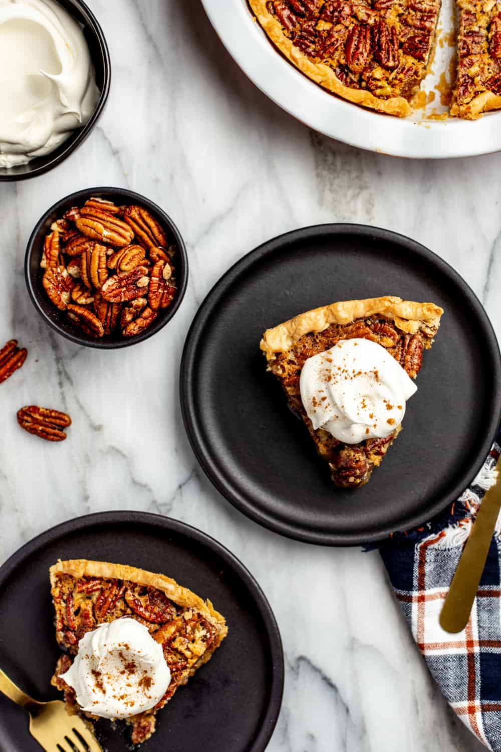 Overhead view of several plated pieces of classic pecan pie, topped with whipped cream