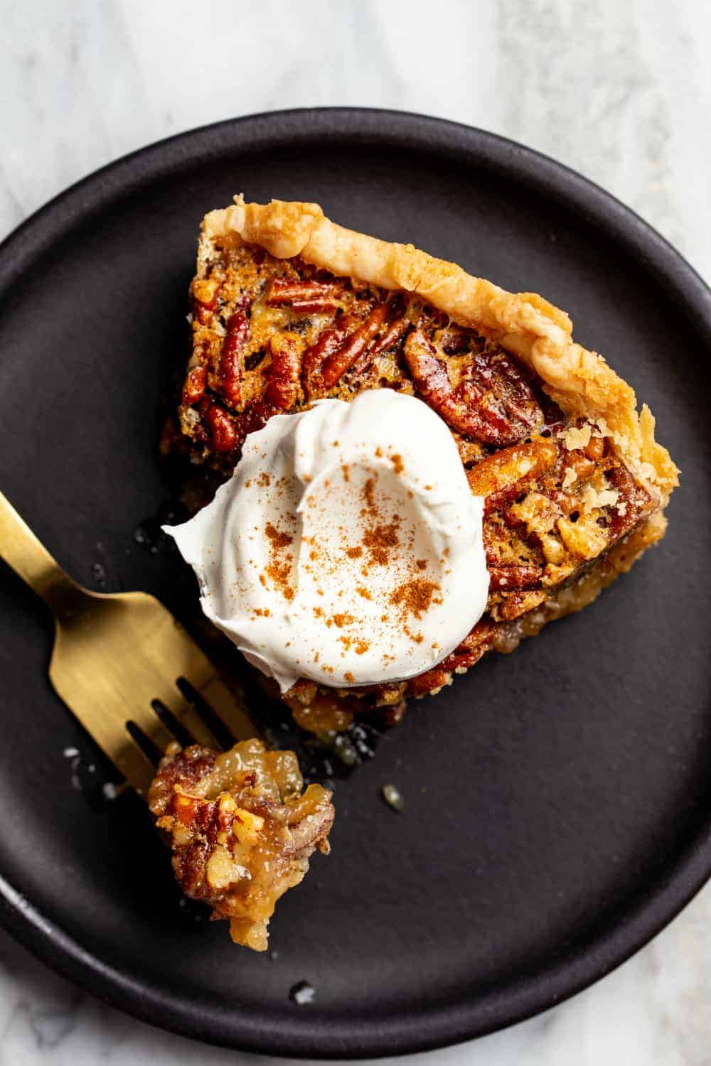 Overhead view of a slice of classic pecan pie on a black plate, topped with whipped cream