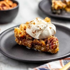 Close up of a slice of pecan pie on a plate, topped with whipped cream