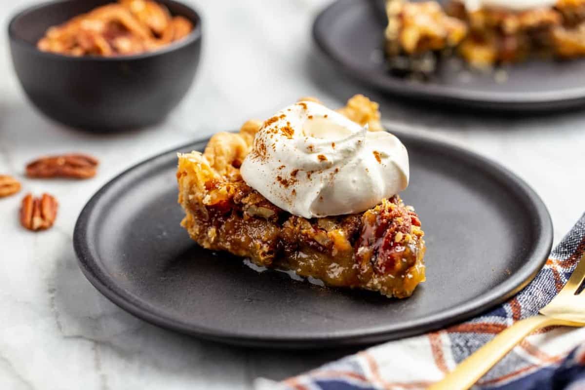 Close up of a slice of pecan pie on a plate, topped with whipped cream