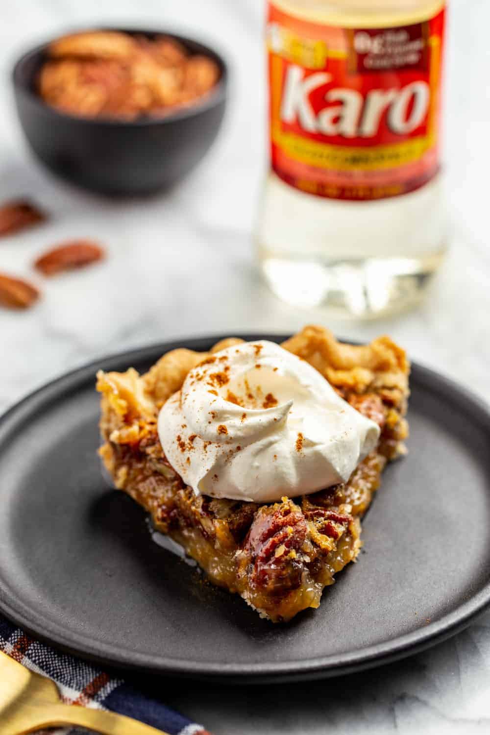 Slice of classic pecan pie on a black plate, topped with whipped cream