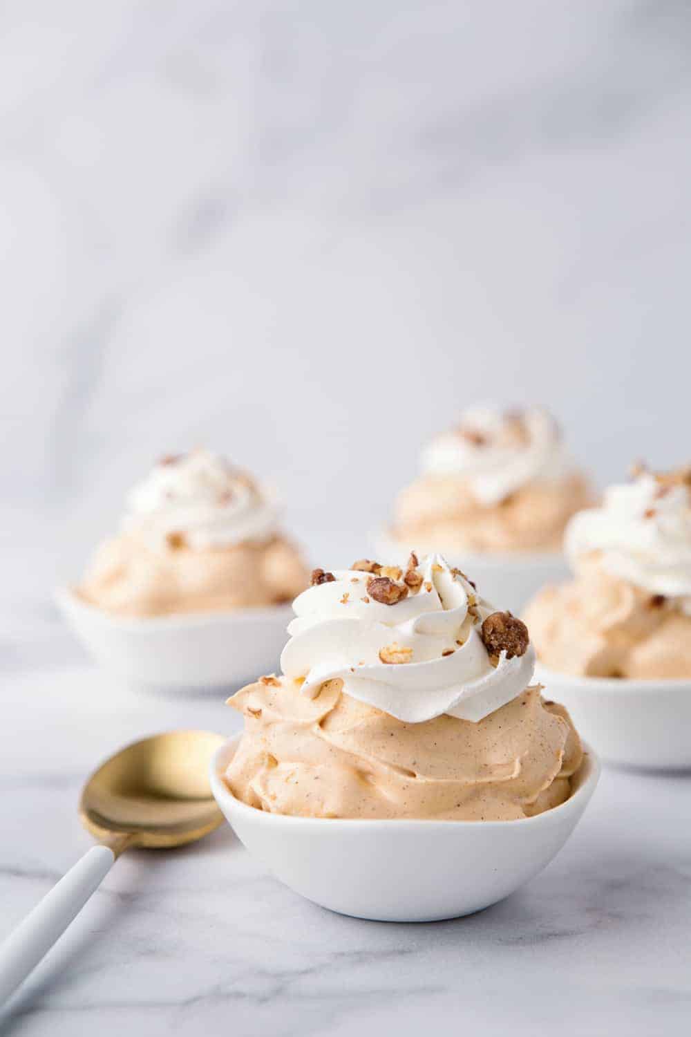 Four bowls of pumpkin spice fluff on a marble surface, garnished with whipped topping