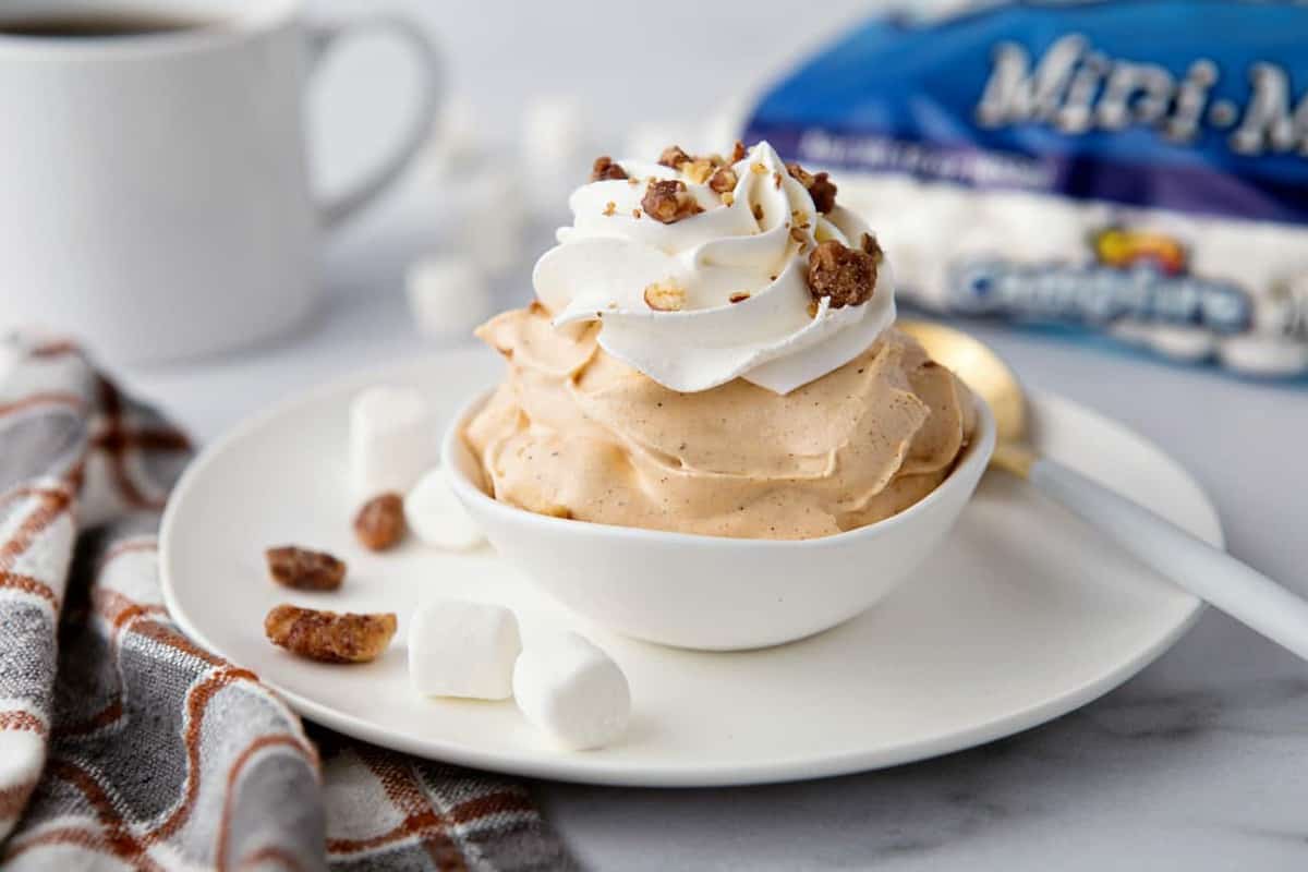 Bowl of pumpkin spice fluff with a cup of coffee and bag of mini marshmallows