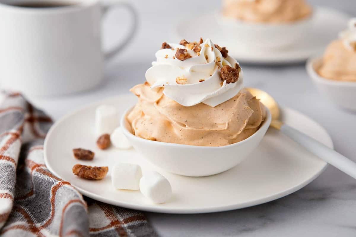 Close up of a white bowl of pumpkin spice fluff garnished with whipped topping and candied pecans