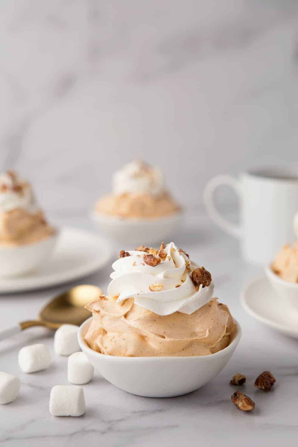 Bowl of pumpkin spice fluff with more bowls and a cup of coffee in the background