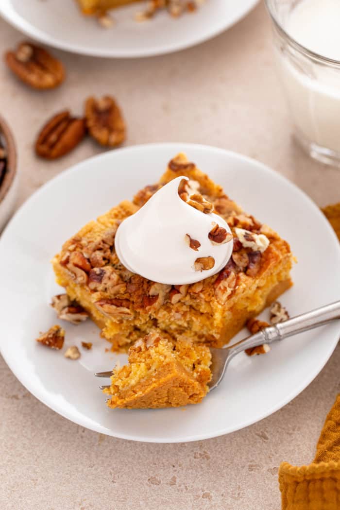 Fork cutting bite from a slice of pumpkin crunch cake on a white plate.