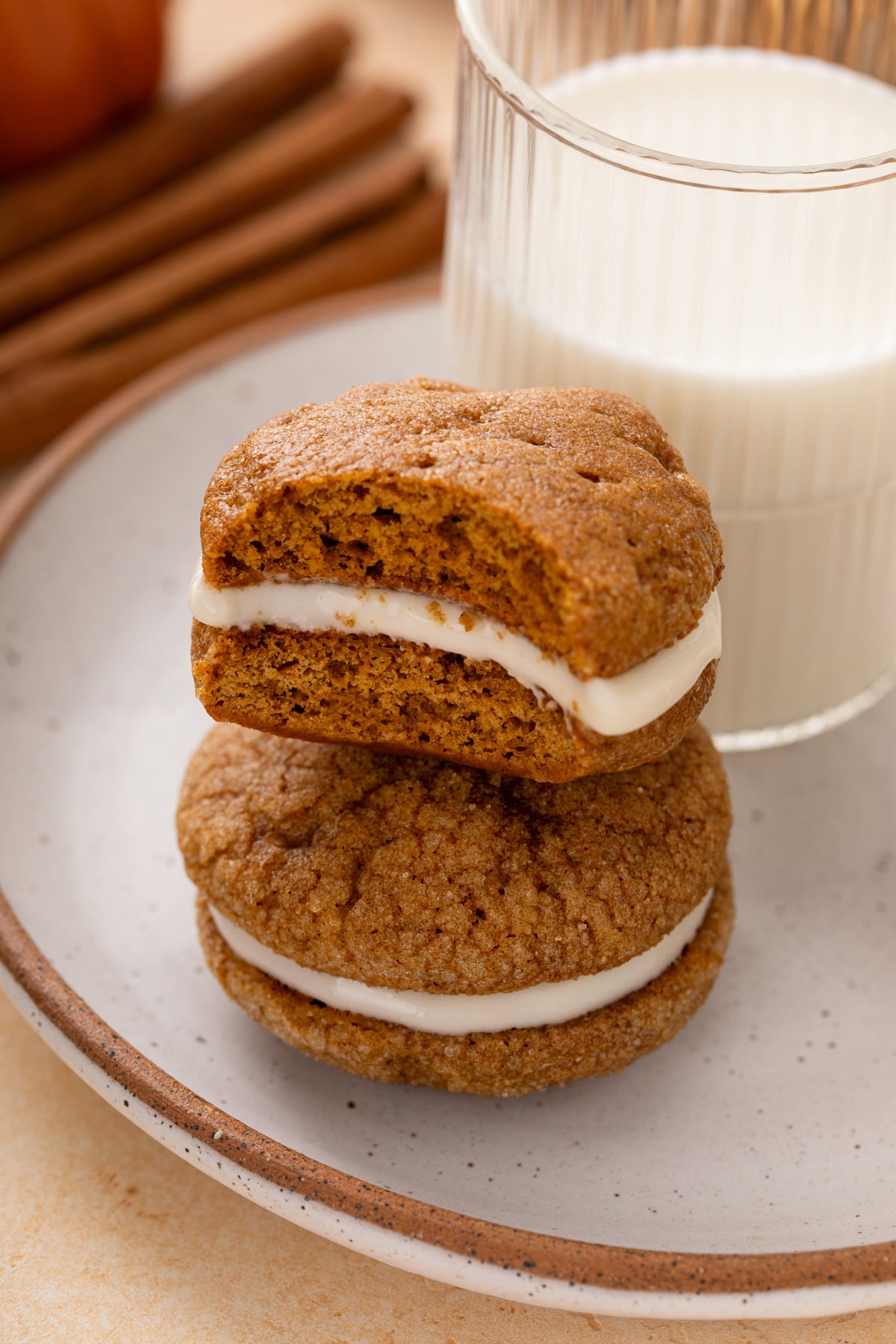 Two pumpkin molasses sandwich cookies stacked next to a glass of milk, with a bite taken from the top cookie.