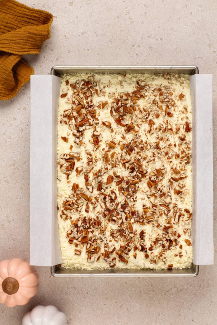 Cake mix and pecans sprinkled on top of pumpkin crunch cake base in a cake pan.