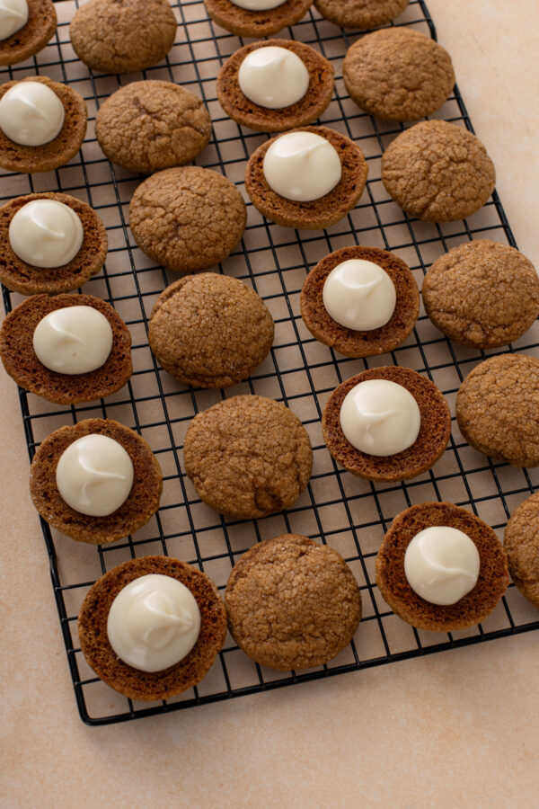 Cream cheese filling piped onto the bottoms of overturned pumpkin molasses cookies, ready to turn them into sandwich cookies.