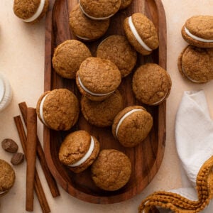 Overhead view of a batch of pumpkin molasses sandwich cookies on a wooden platter.