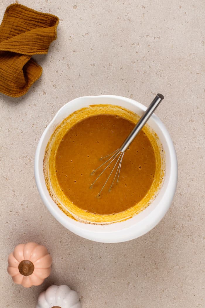 Wet ingredients for pumpkin crunch cake whisked in a white bowl.