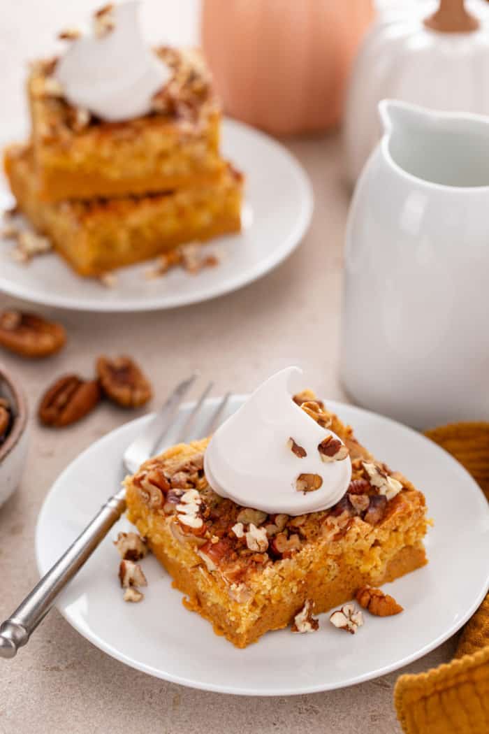 Slice of pumpkin crunch cake topped with a dollop of whipped cream on a white plate.