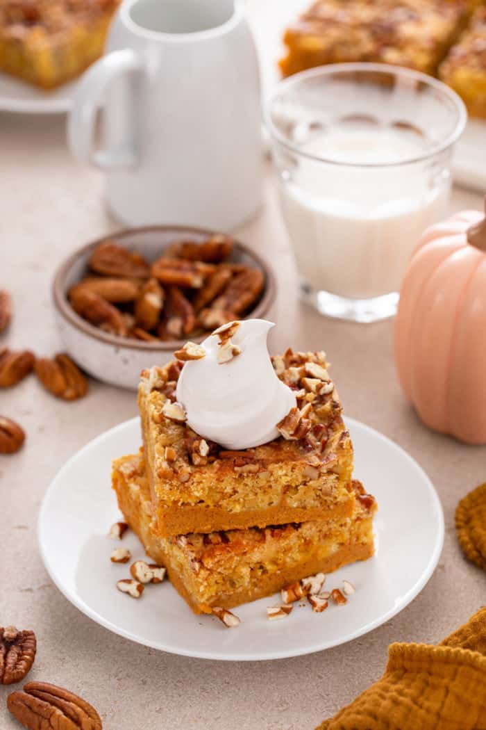 White plate holding two slices of stacked pumpkin crunch cake, topped with a dollop of whipped cream.