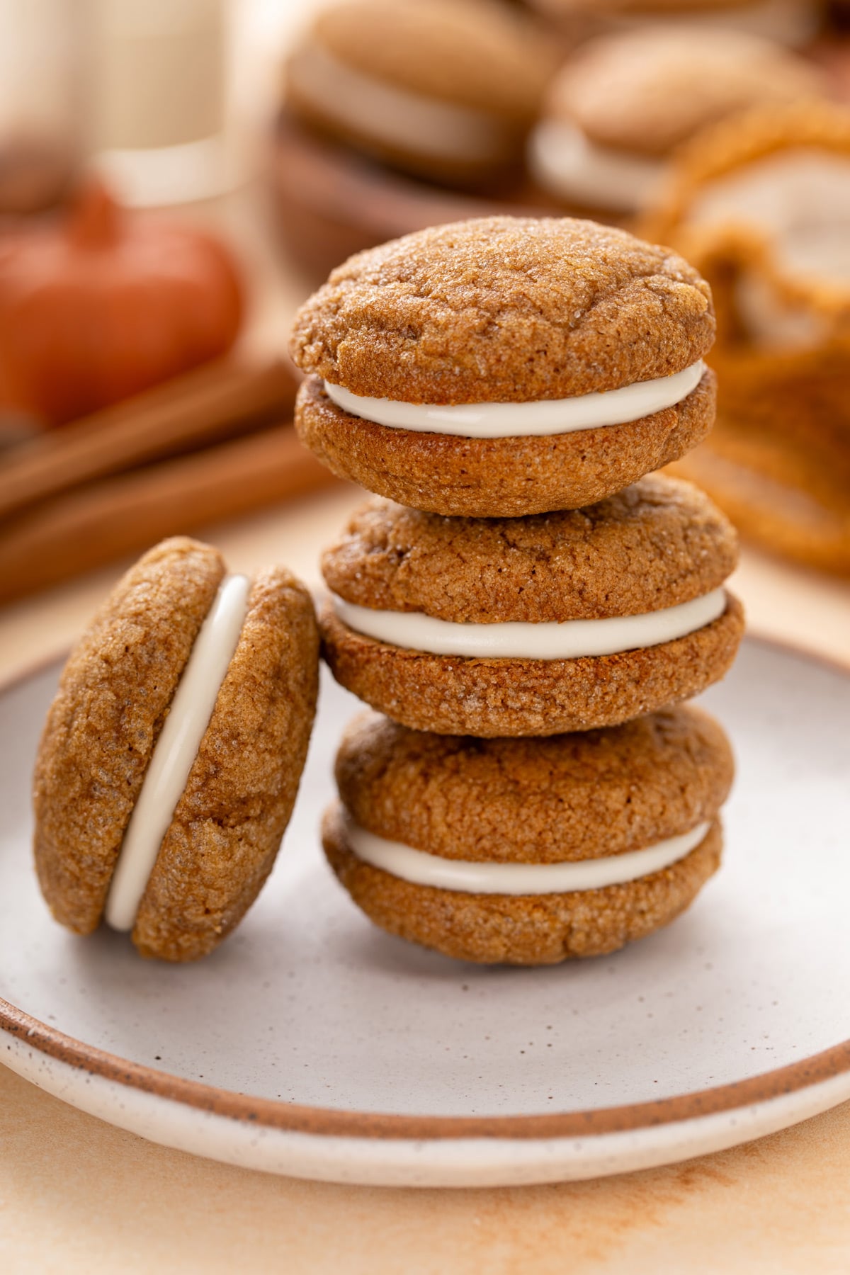 Three pumpkin molasses sandwich cookies stacked on a white plate with a fourth cookie leaning against the stack.