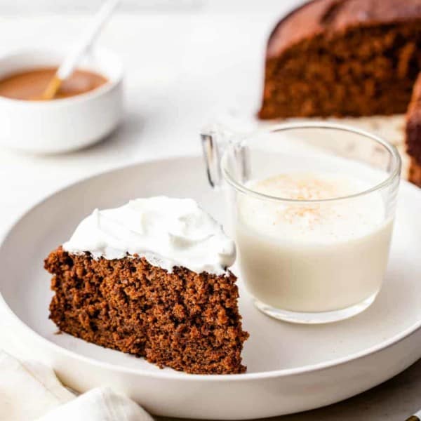 Slice of gingerbread cake and a glass of eggnog on a white plate