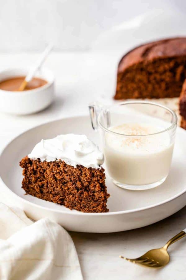Slice of gingerbread cake and a glass of eggnog on a white plate