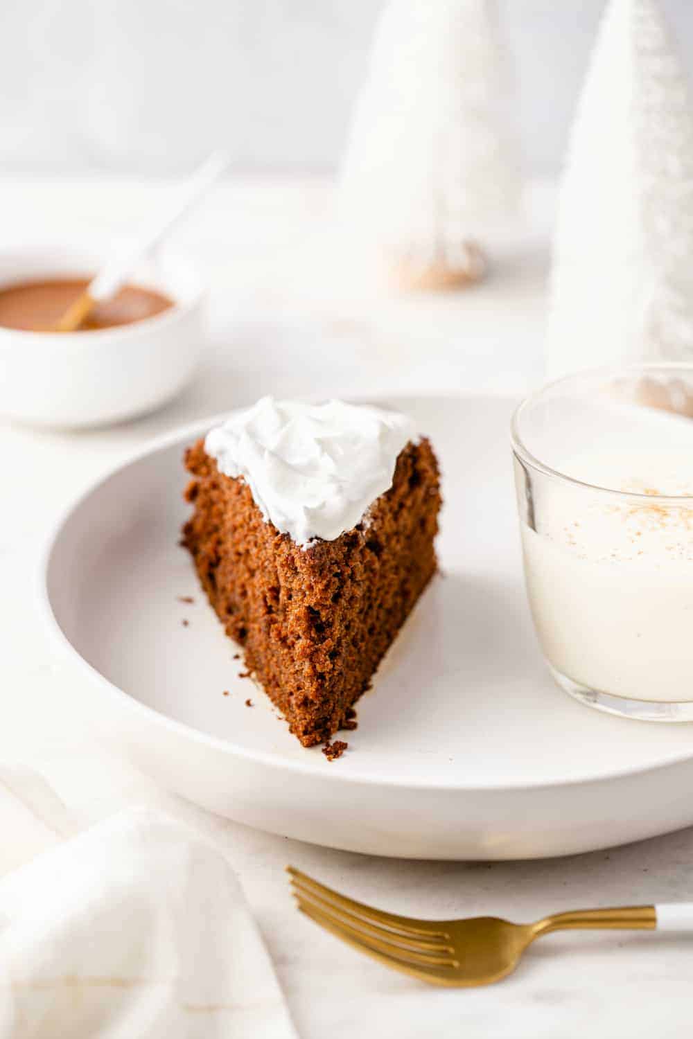 Glass of eggnog and a slice of gingerbread caked topped with whipped cream on a white plate