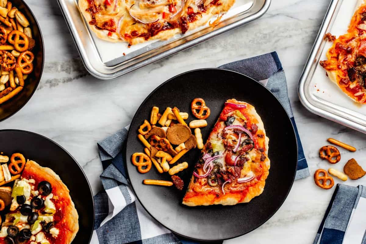 Homemade pizza on a black plate next to snack mix