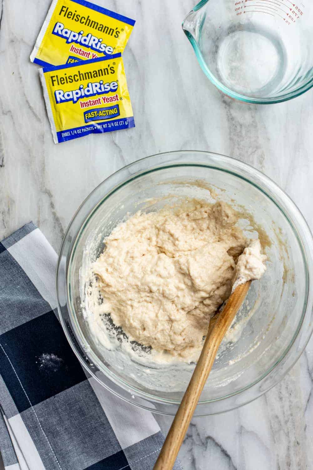 Spoon stirring the dough for 30 minute pizza crust in a glass mixing bowl