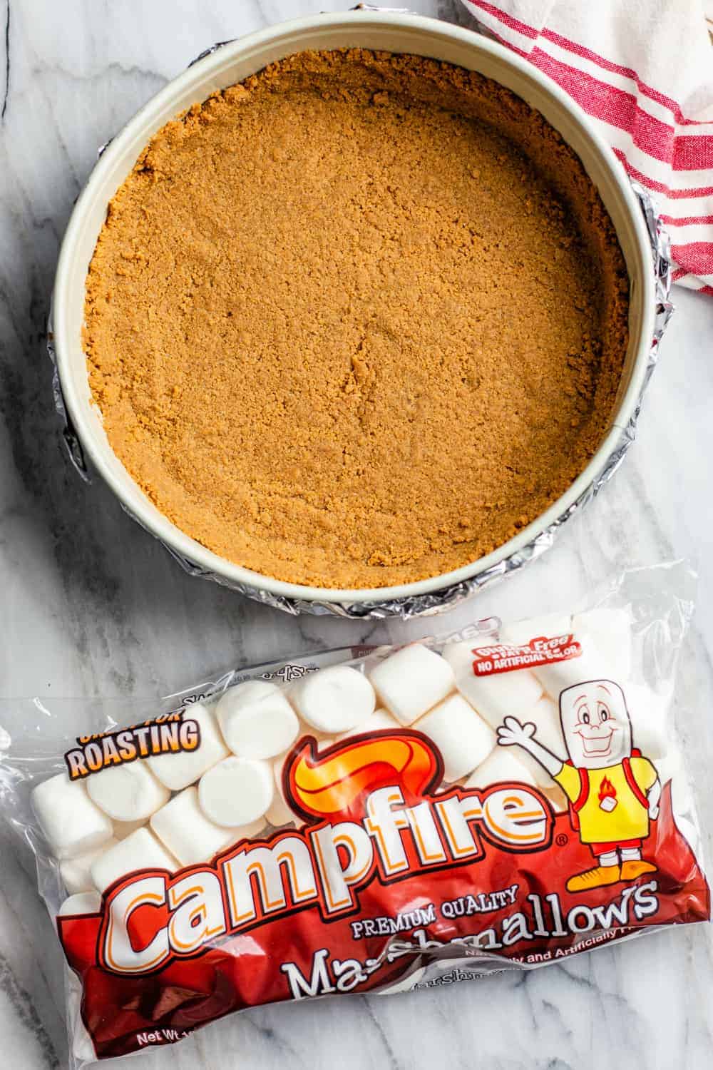 Graham cracker crust in a springform pan next to a bag of marshmallows