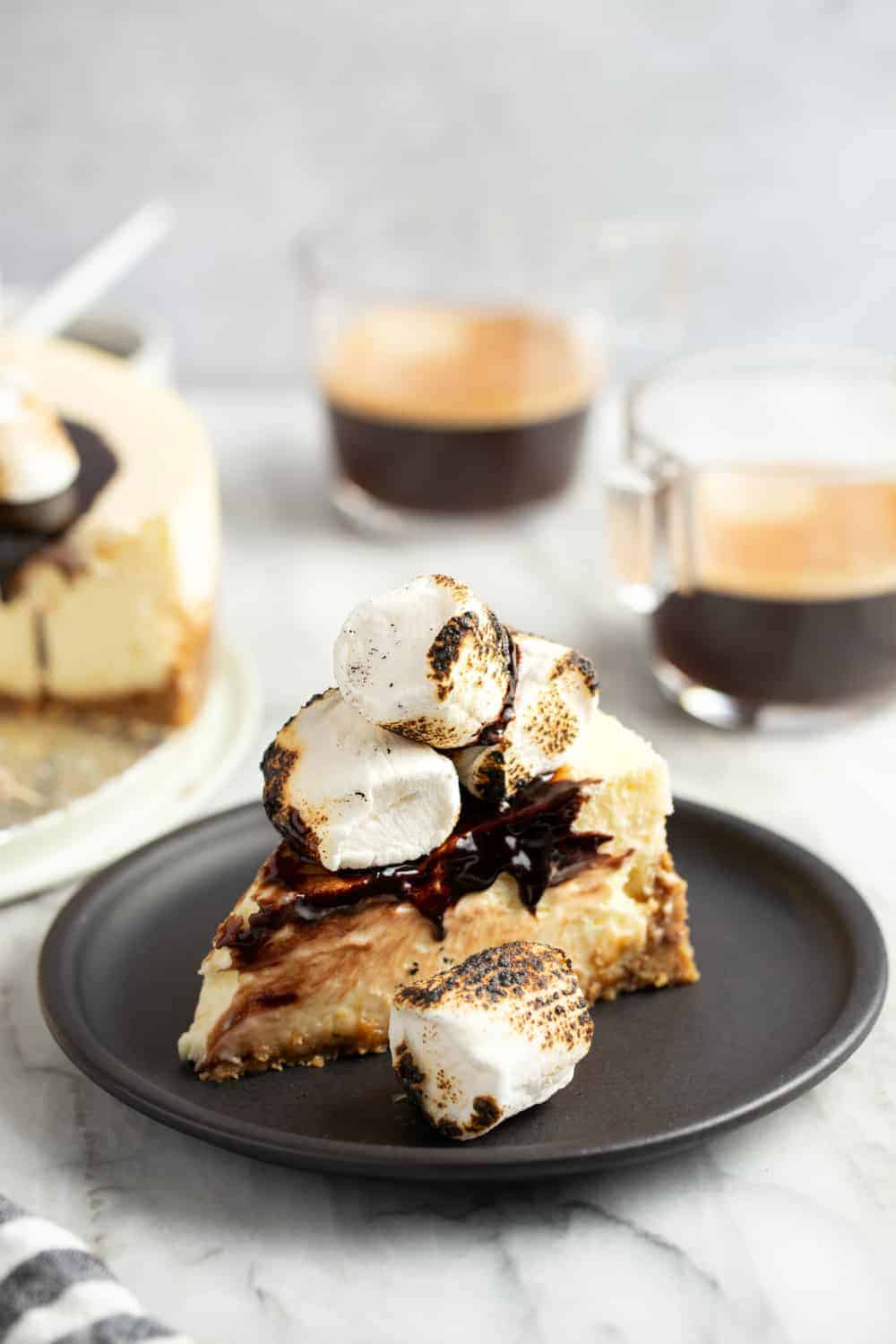 Slice of s'mores cheesecake on a plate in front of cups of espresso