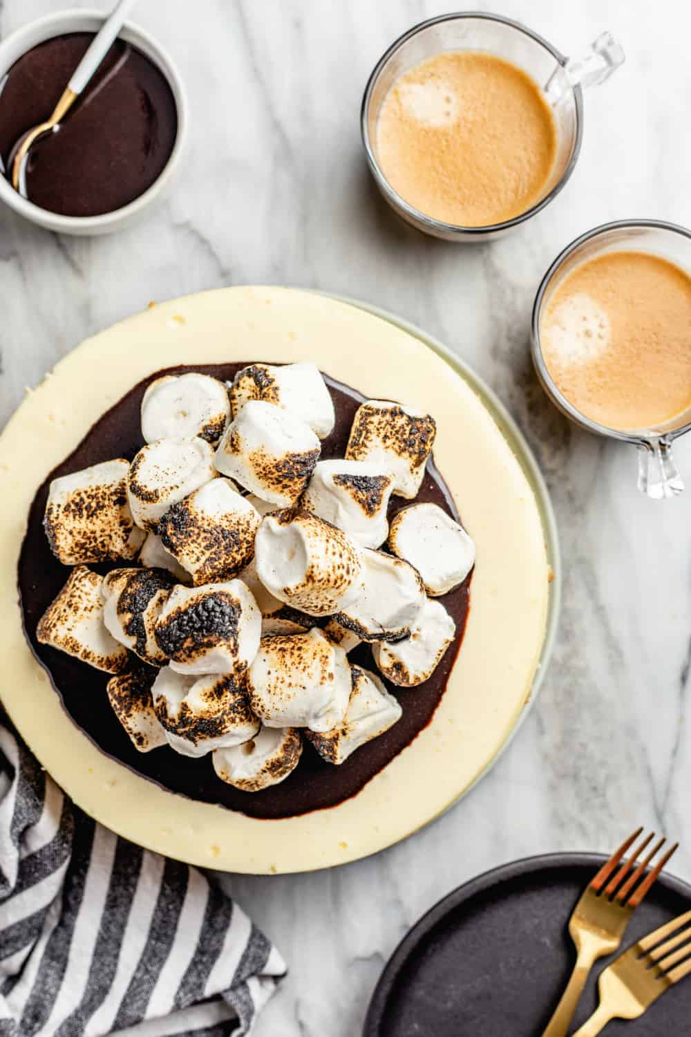cheesecake topped with fudge sauce and toasted marshmallows on a marble surface