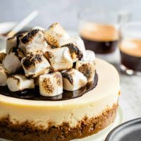 S'mores cheesecake topped with toasted marshmallows in front of cups of espresso