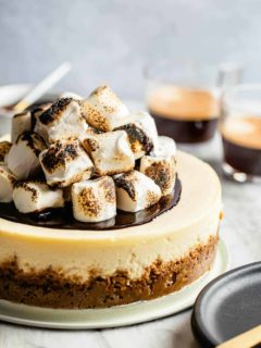 S'mores cheesecake topped with toasted marshmallows in front of cups of espresso